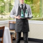 Uncommon Chef 3041 Black Customizable Poly-Cotton Twill V-Neck Tuxedo Apron with Adjustable Neck Strap and 2 Pockets - 28